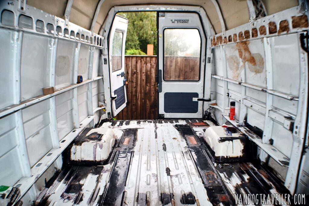 The van as bought — bare rusted metal shell, forklift damage visible down one side, no interior fitted.